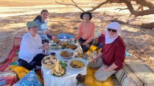 un grupo de personas sentadas alrededor de una mesa con comida en Atta Desert Camp, en El Gouera