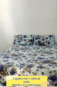 a bed with blue flowers on it with a sign on it at Casa p/ temporada, praia guaibim in Guaibim