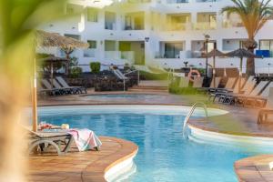 - une piscine avec une table et des chaises à côté d'un hôtel dans l'établissement Apartamentos Galeon Playa, à Costa Teguise