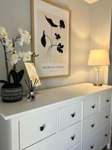 a white dresser with a lamp and flowers on it at Guest Homes - Rice Lane Retreat in Walton on the Hill