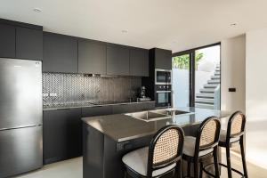 a kitchen with black cabinets and a kitchen island with chairs at Kove Samui in Koh Samui 