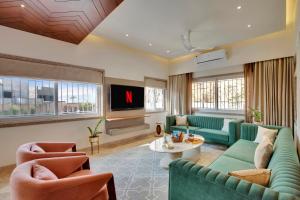 a living room with green couches and a tv at Elivaas Shourya Bliss 3BHK Villa with Pvt Pool, Udaipur in Udaipur