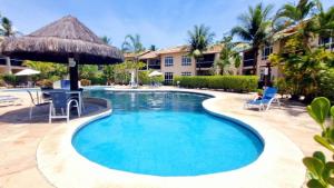 a pool at a resort with chairs and an umbrella at Descanse perto da praia in Porto Seguro