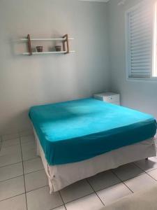 a bed in a white room with a blue blanket at Apto amplo próximo Casa Grande Hotel Resort in Guarujá