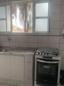 a kitchen with a stove and a sink and two windows at Apto amplo próximo Casa Grande Hotel Resort in Guarujá