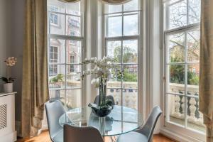 Renovu Premium Homes in Kensington في لندن: غرفة طعام مع طاولة زجاجية وكراسي ونوافذ