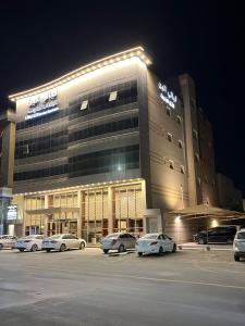 un gran edificio con coches estacionados en un estacionamiento en ليالي الين للشقق المخدومة, en Buraidah