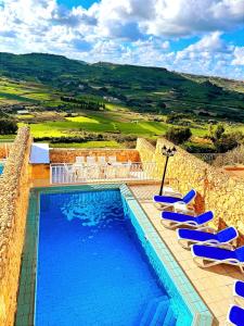 una piscina con sedie a sdraio blu e una montagna di Ortensia a Taʼ Bullara
