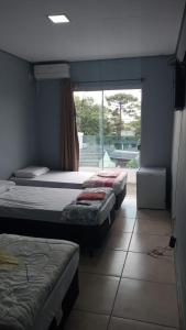 three beds in a room with a large window at Hotel Caçula São Gabriel in São Gabriel