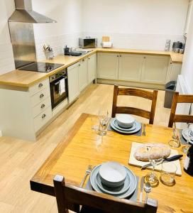 een keuken met een houten tafel met borden en wijnglazen bij Cowpasture Apt - Ilkley Central in Ilkley