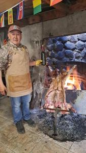 Ein Mann in einer Schürze steht neben einem Grill in der Unterkunft Cabañas El Diamante in Villa Maniguales