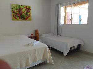 two beds in a white room with a window at Pousada Canto das Estrelas in Chapada dos Guimarães