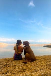 Due persone sedute sulla spiaggia con un cane di Mila Pet friendly house with private beach place a Pag