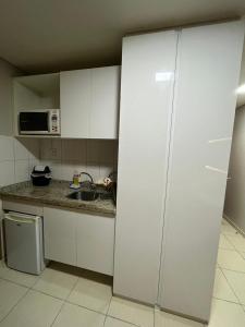 cocina con armarios blancos, fregadero y microondas en Suíte luxo com tela de cinema no América Towers Studio Residence, en Salvador