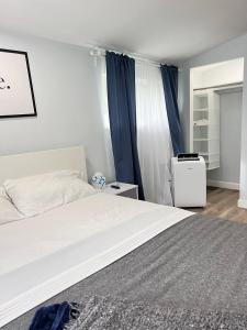 1 dormitorio con cama blanca y cortinas azules en Work, Rest and Play: WiFi, TV and Backyard Bliss en North Miami Beach