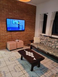 een woonkamer met een bank en een tv aan een bakstenen muur bij Pousada da Sissi in Itanhaém