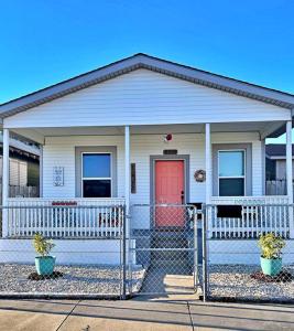 una casa blanca con una puerta roja y una valla en The Poolside Bungalow en Galveston