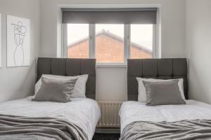 two beds sitting next to a window in a bedroom at Large cosy house w/driveway 7pax in Radcliffe