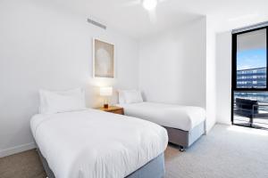 two beds in a white room with a window at Village Palm Beach - Brand New 2 Bedroom Apartment in Gold Coast