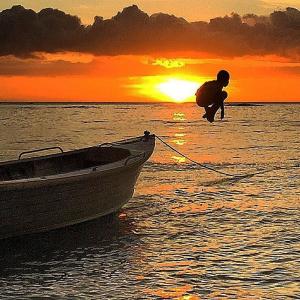 Un uomo sta tirando una barca in acqua al tramonto di Mai Sunset Island Resort a Naviti Island
