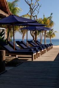 a row of benches with umbrellas on a beach at Meno House - Adults Only in Gili Meno