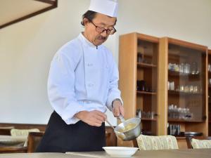 un hombre con un sombrero de chef revolviendo un tazón en Petit Hotel Kanan, en Chino