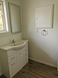 a white bathroom with a sink and a mirror at Sunshine hillcrest home in Auckland