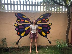 a woman standing in front of a butterfly painted on a wall at Shree Hari Guest House in Anjuna