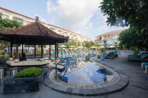 a resort with a swimming pool with tables and umbrellas at Kuta Beach Club Hotel in Kuta