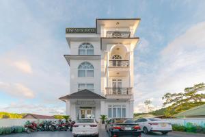 PINE VIEW Hotel Dalat في دالات: مبنى ابيض فيه سيارات تقف امامه