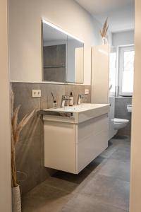 W białej łazience znajduje się umywalka i lustro. w obiekcie ApartHome - LUXUS PUR auf 91m2 Klima w mieście Eching