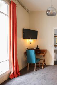 um quarto com uma secretária com uma cadeira azul e uma televisão em Hôtel Des Batignolles em Paris