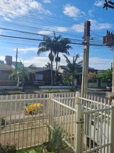 a white fence with a yellow car in the street at Aluguel de quarto in Torres