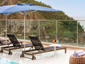 - une piscine avec 2 chaises et un parasol bleu dans l'établissement Novotel Rio de Janeiro Leme, à Rio de Janeiro
