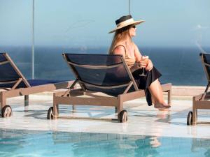 Una donna seduta su una sedia accanto a una piscina di Novotel Rio de Janeiro Leme a Rio de Janeiro