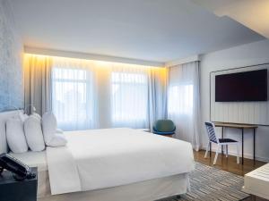 um quarto de hotel com uma grande cama branca e uma televisão em Novotel Rio de Janeiro Leme no Rio de Janeiro