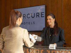 a woman handing a woman a piece of paper at Mercure Prishtina City in Pristina