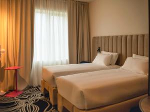 two beds in a hotel room with a window at TRIBE Milano Malpensa in Vizzola Ticino