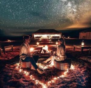 two people sitting around a fire pit under a starry sky at Fantastic Desert Luxury Camp in Merzouga