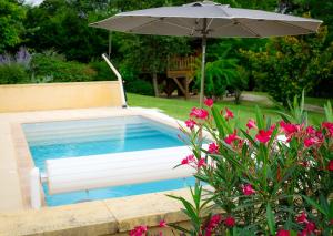 una piscina con sombrilla y flores rosas en Les Chalets du Brusquand en Marquay