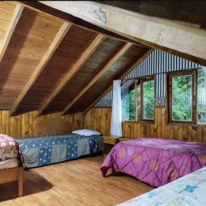 two beds in a room with wooden walls and windows at Cabaña Pachamama in Caburgua