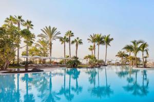 a large swimming pool with palm trees in the background at Tivoli La Caleta Resort in Adeje