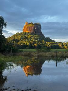 una formación rocosa con su reflejo en un cuerpo de agua en Mango Villa Sigiriya, en Sigiriya