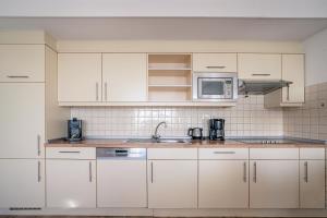 Una cocina blanca con gabinetes blancos y un fregadero. en Appartementencomplex Juliana 124, en De Koog