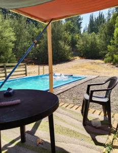 una mesa y una silla bajo una sombrilla junto a la piscina en Casa campo camino a pelluhue en Cauquenes