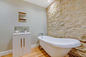 a white bath tub in a bathroom with a stone wall at The Old Workshop in Stow on the Wold +15 photos