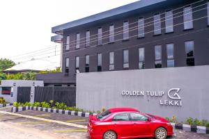 un coche rojo estacionado en un estacionamiento frente a un edificio en Golden Tulip Lekki, en Lekki