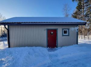 un pequeño cobertizo con una puerta roja en la nieve en Sjöställe Gudö, annexet en Vendelsö