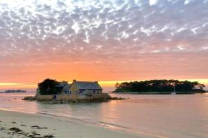 a house on an island in the water at sunset at Maison 6 personnes vue mer in Plougrescant