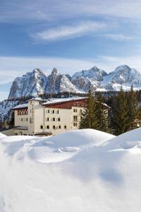 a building in the snow with mountains in the background at B&B Hotel Passo Tre Croci Cortina in Cortina dʼAmpezzo